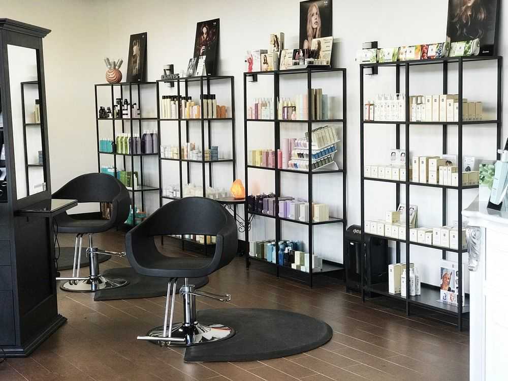 Modern hair salon with black chairs, product shelves, and wooden floors.