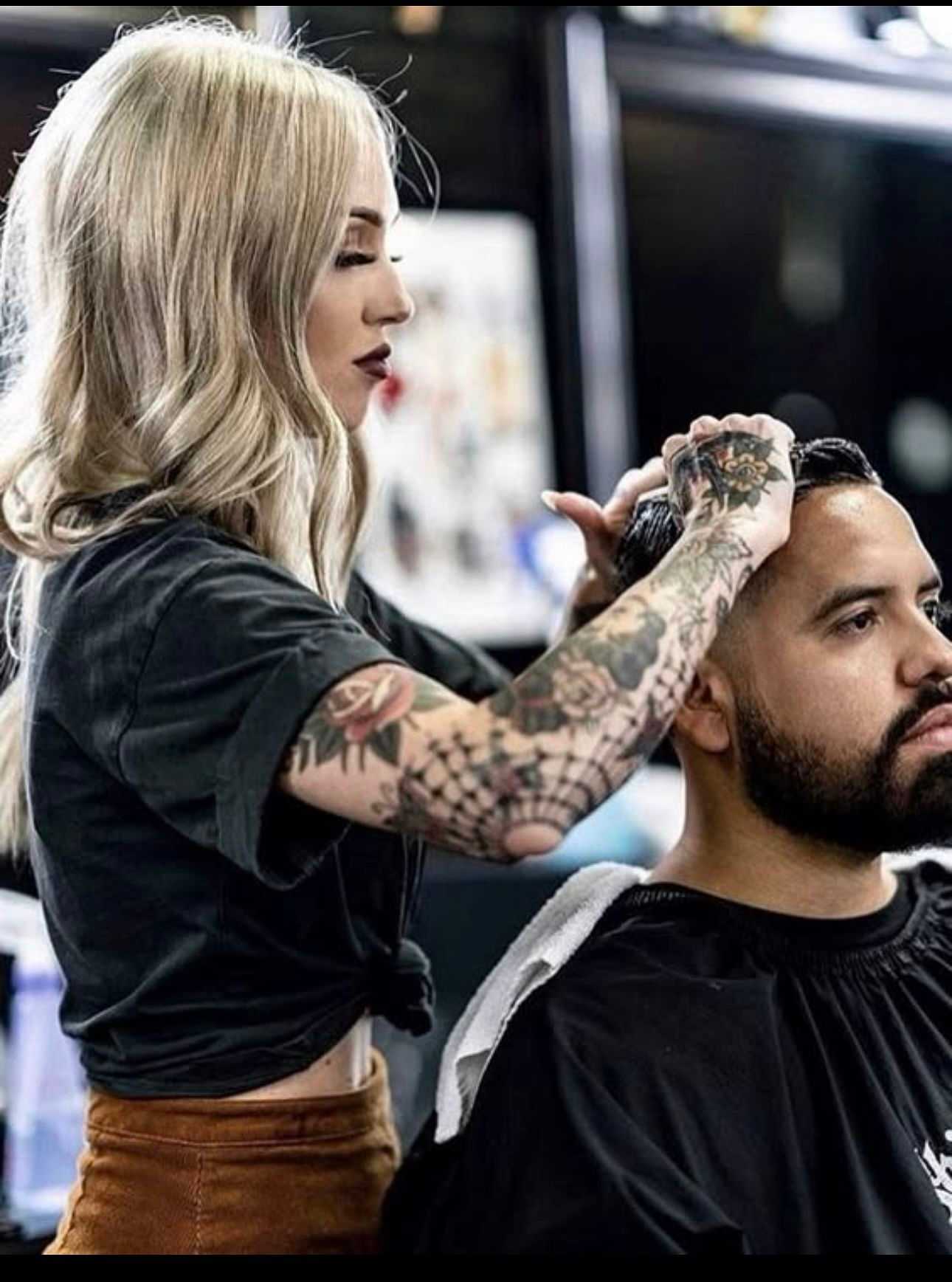 Female barber with tattoos styling a man's hair in a barbershop.